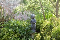 Statue décorative d'enfant parmi le feuillage mixte pour la texture dans le jardin clos