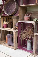 Stockage de caisses en bois vintage avec divers pots, bottes de jardin, un arrosoir rustique et des têtes de graines d'Allium