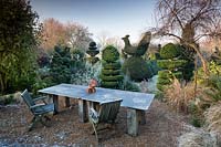 Table et chaises et topiaire if et boîte à Charlotte et Donald Molesworth's garden, Kent, UK.