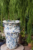Grande urne face à des morceaux de porcelaine bleue et blanche brisée entourée d'un genévrier pleureur. Jardin du sculpteur et céramiste Marcia Donahue à Berkeley, Californie.