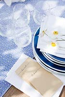 Vaisselle bleue et serviettes blanches avec poches pliées pour y mettre une carte de visite pour habiller la table