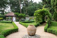 Portail avec glycine sur une pergola, avec haie Buxus sempervirens bordant un chemin de gravier avec pot en terre cuite dans un jardin conçu par Tom Hoblyn à Heatherbrae
