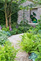 Le jardin Morgan Stanley - chemin de gravier à travers le côté du jardin menant à la sculpture en alcôve dans le mur de pierres sèches, sculpture de Craig Schaffer. La plantation comprend Primula beesiana, hostas et fougère royale.
