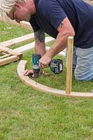 Faire une arche - Un homme perce des trous dans l'arche pour s'adapter aux montants en bois