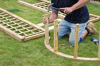 Faire une arche - Homme utilisant un marteau pour fixer les entretoises en bois dans l'arche