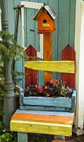 Une chaise en bois colorée avec un pot planté de bégonia