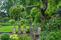 Terrasse menant à la pelouse et au jardin avec une pelouse bien tondue entourée de parterres de fleurs mélangés conçus pour inclure des plantes qui prospèrent à mi-ombre