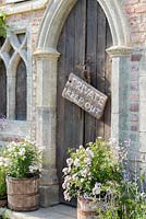 Une entrée gothique flanquée de tonneaux en bois recyclé plantés de roses.