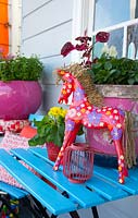 Table à lattes bleu vif avec des pots roses et un cheval rouge peint avec un motif floral, août.
