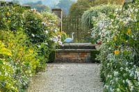 Chemin de gravier, piscine surélevée, porte et sculpture d'oiseau héron par Michael Lythgoe - Bourton House Garden, Gloucestershire