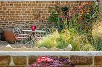 Petite cour avec jardin et table et chaises, Stipa tenuissima, Cirsium rivulare 'Atropurpureum', Cercis canadensis 'Ruby falls'