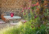 Petite cour avec jardin et table et chaises, Stipa tenuissima, mur de pierre, Cirsium rivulare 'Atropurpureum', Cercis canadensis 'Ruby Falls'