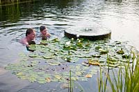 Homme et garçon dans une piscine 'naturelle' regardant des nénuphars