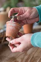 Close up detail de l'utilisation d'un morceau de ficelle noué autour d'une brindille pour attacher un pot en terre cuite à la base de la couronne naturelle