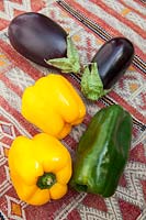 Légumes frais colorés - poivrons jaunes et verts aux aubergines sur une table couverte de kilim