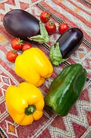 Légumes frais colorés - poivrons jaunes et verts avec aubergines et tomates cerises sur une table couverte de kilim
