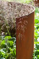 Jardin contemporain avec panneau courbé en acier corten rouillé et herbes Deschampsia cespitosa 'Bronzeschleier' RHS Hampton Court