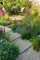 Petit jardin avec dallage en pierre sinueuse, chemin de gravier et coin salon, et parterres de fleurs et d'herbes