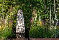 Jardin contemporain avec sculpture en pierre dans une piscine d'eau rectangulaire