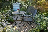 Petit jardin de style chalet d'été avec terrasse en brique, table et chaises en métal et plantation en argent blanc et bleu.