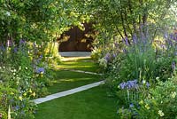 Chemin blanc traversant une pelouse en diagonale, avec des parterres d'arbres et de vivaces. Le jardin A Dogs Life, RHS Hampton Court Show