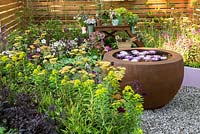 Petit jardin d'été avec vivaces à fleurs et bol d'eau rond avec des nénuphars. Entouré d'une clôture en panneaux de bois