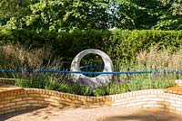 Sculpture circulaire et mur de briques de jardin incurvé avec garde-corps bleu et herbes. Designer Rae Wilkinson