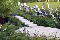 Cancer Research UK Garden Andy Sturgeon Chelsea Show Garden avec feuillage de fougère arborescente, plantation pérenne, mur d'anneaux en acier