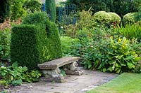Barnsley House Gardens, Gloucestershire, Royaume-Uni. assise en pierre avec 'dossier' topiaire