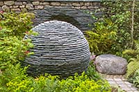 Le Chelsea Flower Show 2005, Londres, Royaume-Uni. 'Le Jardin Philosophique' (Andy Loudon) sphère de pierre avec image négative d'elle-même dans le mur de pierres sèches derrière. Plantation de bois au printemps