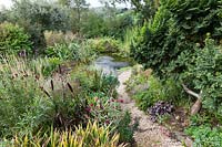 Derry Watkins Garden at Special Plants, Bath, Royaume-Uni. Chemin de gravier menant à un étang de taille moyenne