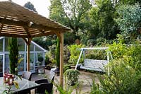 Le jardin de Jackie Healy près de Chepstow. Jardin au début de l'automne. 'Pergola' en bois de style japonais et banc de balançoire dans le patio