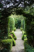 Owlpen Manor, Gloucestershire, Royaume-Uni. Automne, vue à travers l'arche d'if vers le jardin topiaire