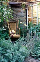 Chaise en rotin avec chapeau de paille dans un coin d'un petit jardin clos