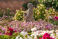 Rosa - David Austin roses dans des parterres de fleurs, comme la R. à fleurs roses 'Harlow Carr' entourant la sculpture avec des arcs supportant les rosiers grimpants