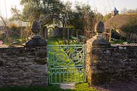 Porte d'accès au jardin de coupe où un chemin d'herbe mène sous quatre poutres blanches dressées, Sorbus aria 'Lutescens', vers une porte d'accès au potager. Ferme Brilley Court, Whitney-on-Wye, Herefordshire