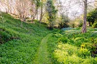 Chemin d'herbe à travers le jardin de la vallée, menant vers un pont peint en bleu sur le ruisseau, Brilley Court Farm, Whitney-on-Wye, Herefordshire, Royaume-Uni.
