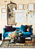 Un mur d'illustrations encadrées derrière un canapé bleu, une table et des fleurs fraîches.