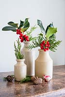 Coupez Ilex avec des baies exposées dans des vases en grès et des accessoires d'hiver séchés à la maison.