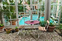 Une table et des chaises de bistrot sont installées devant la piscine intérieure. Marina Wüst garden, Allemagne.