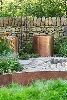 Sièges en cuivre entourés d'un mur en pierre sèche. Le Warner Edwards Garden, une représentation de Falls Farm dans la campagne du Northamptonshire, parrain: Warner Edwards, RHS Chelsea Flower Show, 2018.