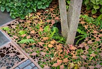 Pavage perméable en forme de feuille fait de grilles métalliques découpées au laser sur la plantation de fougères. Jardin Urban Flow, commanditaire: Thames Water, RHS Chelsea Flower Show, 2018.