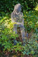 Sculpture de figure féminine assise par Derek Kinzett entouré de plantes à feuillage - Shropshire, Royaume-Uni