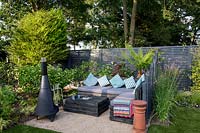 Jardin londonien contemporain avec clôture peinte en gris. Paravent en bois - Coin salon inférieur avec fleur de Chimenea Purple est Verbena bonariensis Tree Fern - Dicksonia Antarctica