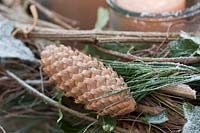 Une couronne de l'Avent sur une table du jardin collée à partir de cônes de Pinus strobus, de pin vert, de lierre Hedera helix, de clématite cirrus, recouverte de neige poudreuse ou de givre blanc. À l'intérieur de la couronne, vous trouverez 4 bougies dans des lanternes.