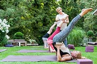 Yoga dans un jardin verdoyant. L'enseignant corrige la position appelée Viparita Karani.