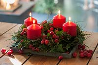 Couronne de Vaccinium myrtillus et cirrus de lierre avec infructescence - Couronne de l'Avent avec 4 bougies rouges et spécification Malus. baies sur la table en bois