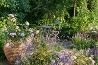 Rosa 'Wildeve', Salvia et Achillea avec table et chaises. 'Le meilleur des deux mondes', RHS Hampton Flower Show 2018