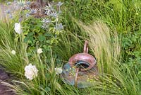 Roses blanches, Stipa et Eryngium avec cruche en cuivre. 'Style and Design Garden', RHS Hampton Flower Show 2018