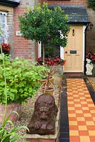Jardin avant de maison mitoyenne victorienne, avec un chemin carrelé à côté d'une zone gravillonnée contenant des statues et des plantes en pot. Le jardin secret de Serles House, Dorset, UK.